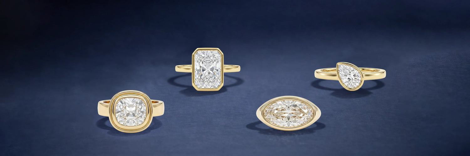 Four bezel-set lab-grown diamond engagement rings in yellow gold — cushion cut, radiant cut, marquise cut flush bezel, and pear cut solitaire on dark blue background