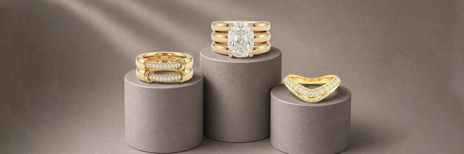 Three designer lab-grown diamond bands in yellow gold — bold chunky pavé bar ring, triple stacked wide oval solitaire band, and curved chevron pavé band with fancy yellow diamond accents on grey cylinder pedestals
