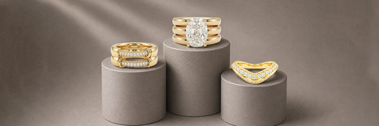 Three designer lab-grown diamond bands in yellow gold — bold chunky pavé bar ring, triple stacked wide oval solitaire band, and curved chevron pavé band with fancy yellow diamond accents on grey cylinder pedestals