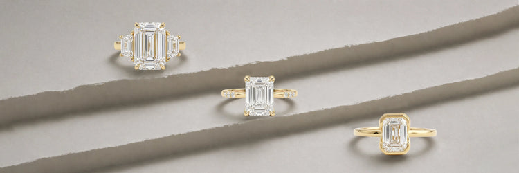 Three emerald cut lab-grown diamond engagement rings in yellow gold — three-stone with trapezoid baguette side stones, classic four-prong solitaire with thin band, and full bezel solitaire on layered stone surface