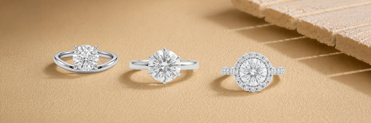 Three round cut lab-grown diamond engagement rings in white gold — bypass solitaire, six-prong classic solitaire, and round brilliant halo with pavé band on sandy beige surface