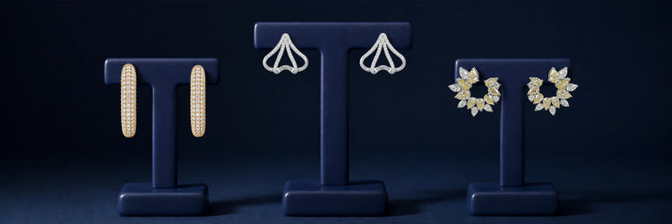 Pairs of lab-grown diamond earrings on navy displays — yellow gold pavé dome hoop earrings, white gold open fan-shaped ear climbers, and yellow gold marquise sunburst open hoop earrings on dark blue background