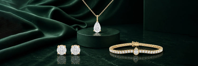 Lab-grown diamond fine jewelry set in yellow gold — pear cut solitaire pendant necklace on dark green pedestal, round brilliant four-prong stud earrings, and round brilliant tennis bracelet with pear cut clasp accent on dark marble surface