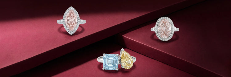 Four fancy colored lab-grown diamond rings in white gold — pink marquise halo, pink oval double halo with baguette shoulders, blue asscher cut solitaire, and fancy yellow pear cut solitaire on burgundy display